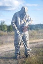 A soldier in a chemical protection suit checks the radioactive territory with a dosimeter against the background of wild vegetatio