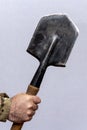 A soldier holds a sharpened sapper shovel in his hand on a light background.