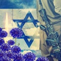 Soldier of Israeli defense forces on Israeli national flag, wall and sky background. Ceremonial burning candle and blue flowers