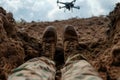 soldier legs laying on the dirt with flying drone in the sky above