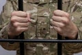 Soldier in military camouflage holding hands to the bars in the courtroom against a light background. Concept: trial of a soldier,