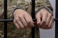 Soldier in military camouflage holding hands to the bars in the courtroom against a light background. Concept: trial of a soldier,