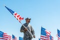 Soldier in military uniform and cap holding american flag while standing against blue sky Royalty Free Stock Photo