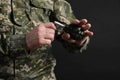 Soldier pulling safety pin out of hand grenade on black background, closeup. Military service Royalty Free Stock Photo