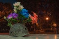 A soldier`s helmet with bullet holes and flowers on an obelisk in memory of fallen soldiers in the light of lanterns