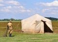 Soldier stands next to an old military tent on the meadow