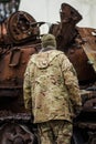 Soldier in uniform near a burnt and melted rusty wreckage of a Soviet Russian-made tank Royalty Free Stock Photo