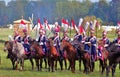 Soldiers in historical costumes hold flags and ride horses.