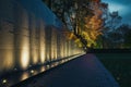 A solemn photo of the Vietnam War Memorial, illuminated by soft lights, with visitors paying their respects, A night scene of the