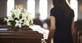 A Solemn Woman with White Lily Flowers Stands by a Coffin During a Funeral Service Royalty Free Stock Photo