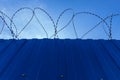 Solid, blue iron fence with barbed wire under a blue sky Royalty Free Stock Photo