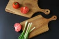 Solid oak wooden cutting boards, chopped green onions and red fresh tomatoes on a black background. Concept of choosing vegetables Royalty Free Stock Photo