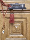 A solid wood door detail with a bronze letterbox and handle, decorated with reddish cord and tassel.