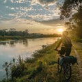 A solitary cyclist pauses to enjoy the golden sunset reflecting on a calm river beside a lush tropical path