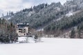 Solitary hotel building in a beautiful snowy winter landscape with forest and frozen dam