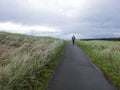 Solitary man walking on a cement path through coastal grasses on a clear cool day