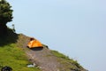 Solitary orange tent camped near water edge