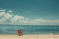 A solitary red chair faces the tranquil blue sea, offering a peaceful retreat under the vast, cloud filled sky