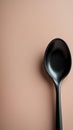 A solitary sleek black spoon on a soft peach-colored background Royalty Free Stock Photo