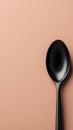 A solitary sleek black spoon on a soft peach-colored background Royalty Free Stock Photo