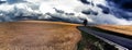 Solitary tree behind asphalt road and agriculture field with dramatic cloudy sky