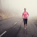 The solitude of an early jog. A young woman jogging on a country road on a misty morning. Royalty Free Stock Photo