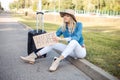 Solitude, upset melancholy blond woman in hat hitchhiking, sit on curb by road, hold carton board anywhere with suitcase