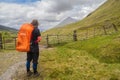 Solo female hiker with orange backpack walking the West Highland Way between Tyndrum and the Bridge of Orchy