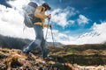 Solo hiker wearing professional and trekking poles walk across sunny mountain track. Young tourist traveling along rocky trek