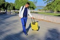 Solo traveling man with yellow luggage on the grass with city park background