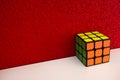 Solved puzzle speed cube on white wooden shelf near red colored wall, colorful rubiks cube with copy space mind challanging Royalty Free Stock Photo