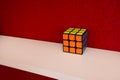 Solved puzzle speed cube on white wooden shelf near red colored wall, colorful rubiks cube with copy space mind challanging Royalty Free Stock Photo