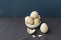 Some eggs lie in white ceramic bowl, one whole egg and eggshell are near on table covered with dark grey fabric,