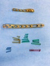 Some explanted titanium screws and titanium plates in different colors and sizes lie on a blue cloth