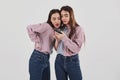 Some interesting content in their phones. Sharing with secrets. Two sisters twins standing and posing in the studio with Royalty Free Stock Photo