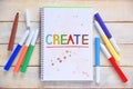 Some markers on a white wooden desktop and a notebook with the word CREATE colorful hand written on it. Royalty Free Stock Photo