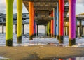 Rainbow colored stone poles under the pier of scheveningen beach the netherlands with sand and waves in the in the sea Royalty Free Stock Photo