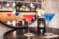 Some red and blue cocktails with sugar and salt on a black table next to a circular mirror