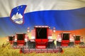Industrial 3D illustration of some red farming combine harvesters on farm field with Slovenia flag background - front view, stop