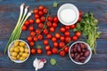 Red fresh tasty cherries, green spring onions, green rosemary, leaves of coriander, sweet cheese, olives, garlic on dark wo