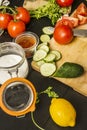 Some ripe split tomatoes along with garlic, cucumber slices, paprika, a bottle of salt, whole lemons, olive oil and a knife on a