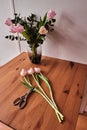 Some tulips and a scissors lie on a wood table