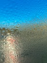 Somebody standing behind wet window with natural water drops on blue glass background. Spring or summer rain drops on car window. Royalty Free Stock Photo