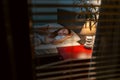 Someone is peeping through the blinds on window at woman lying in bed in her bedroom. Concept of voyeurism and criminal