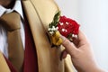 Pinning flowers red rose flower on a man with a golden suit.