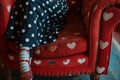 someone in a polkadotted dress on a red armchair with heart motifs