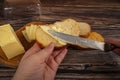 Someone spreads butter on fresh wheat toast with a knife, a wooden butter dish with a piece of butter and slices of cheese on a Royalty Free Stock Photo