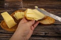 Someone spreads butter on fresh wheat toast with a knife and a wooden butter dish with a piece of butter and slices of cheese on a Royalty Free Stock Photo