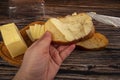 Someone spreads butter on fresh wheat toast with a knife and a wooden butter dish with a piece of butter and slices of cheese on a Royalty Free Stock Photo