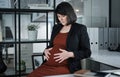 Someone wants to meet mommy early. an attractive businesswoman sitting and feeling stressed while holding her pregnant Royalty Free Stock Photo